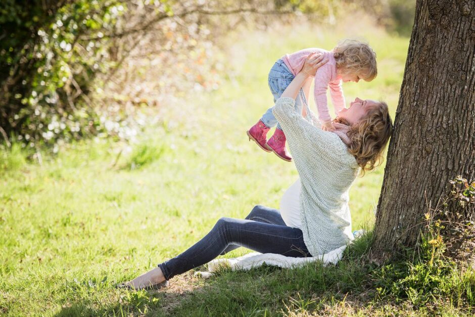 Mom lifting baby under tree. Holistic nutrition includes healthy mothering.