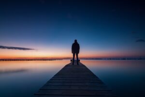 Man standing on a dock staring at the sunrise represents looking within.